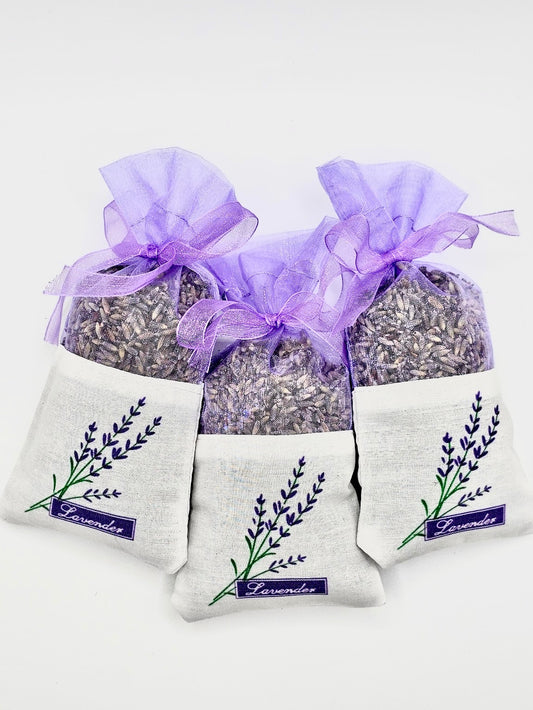 A set of three dried lavender sachets, each with a purple ribbon and a printed lavender design on a white fabric pouch.