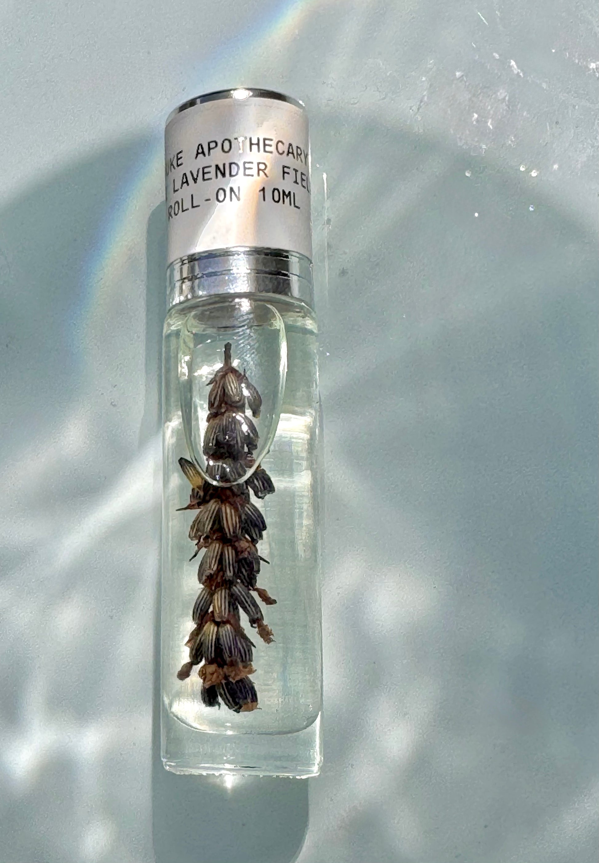 Small glass bottle with lavender flowers and a silver cap on a light background