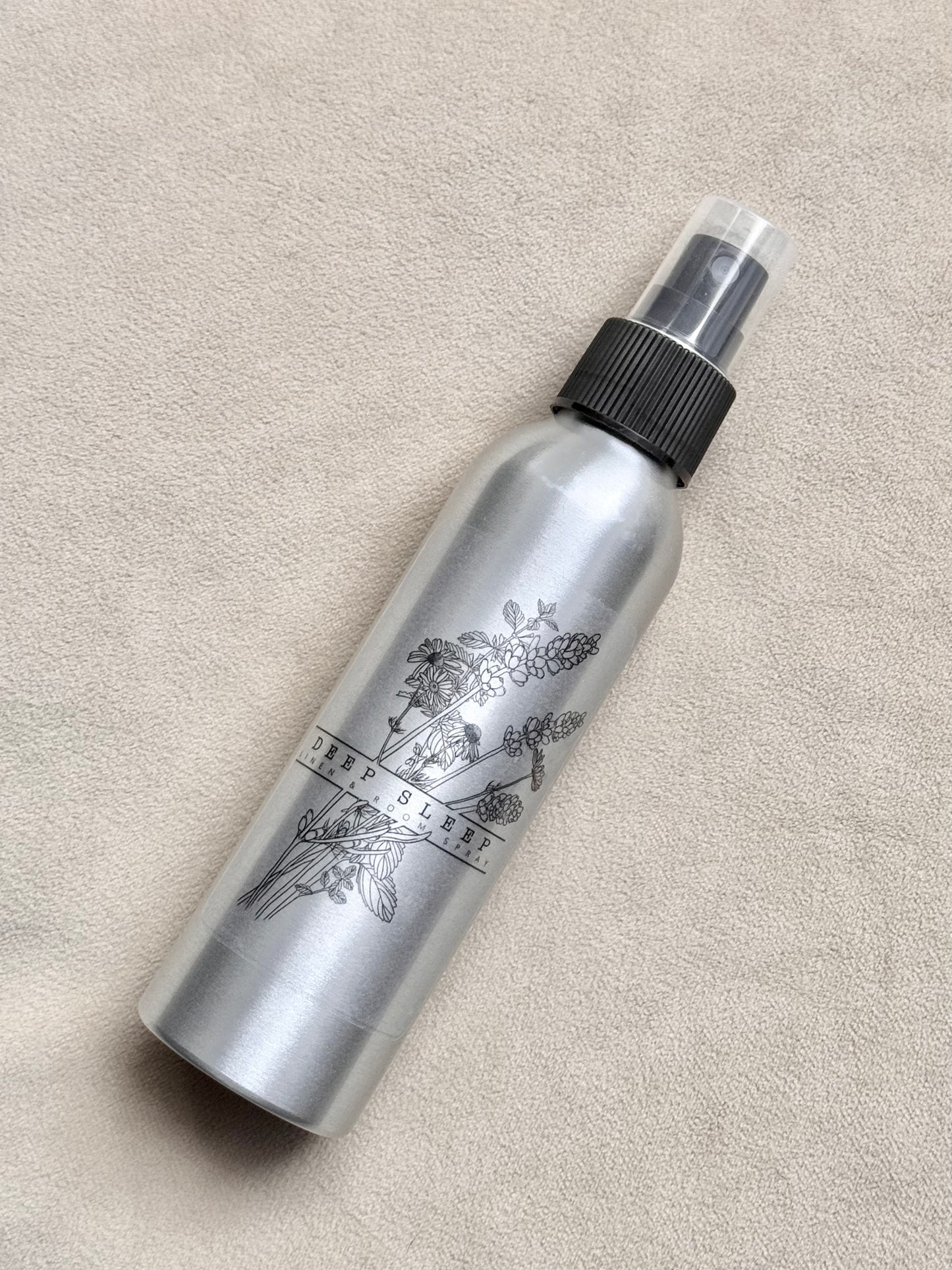 Silver spray bottle with black nozzle on a beige surface