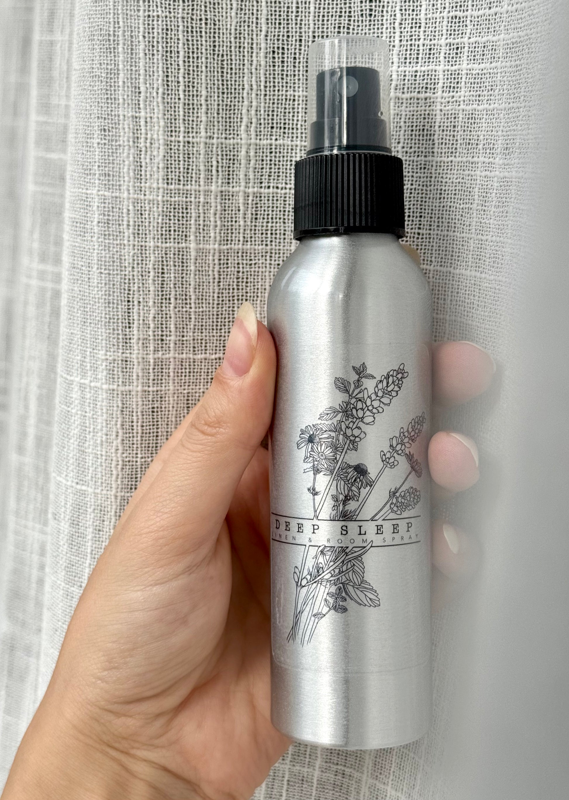 Hand holding a silver spray bottle with black cap against a textured gray background