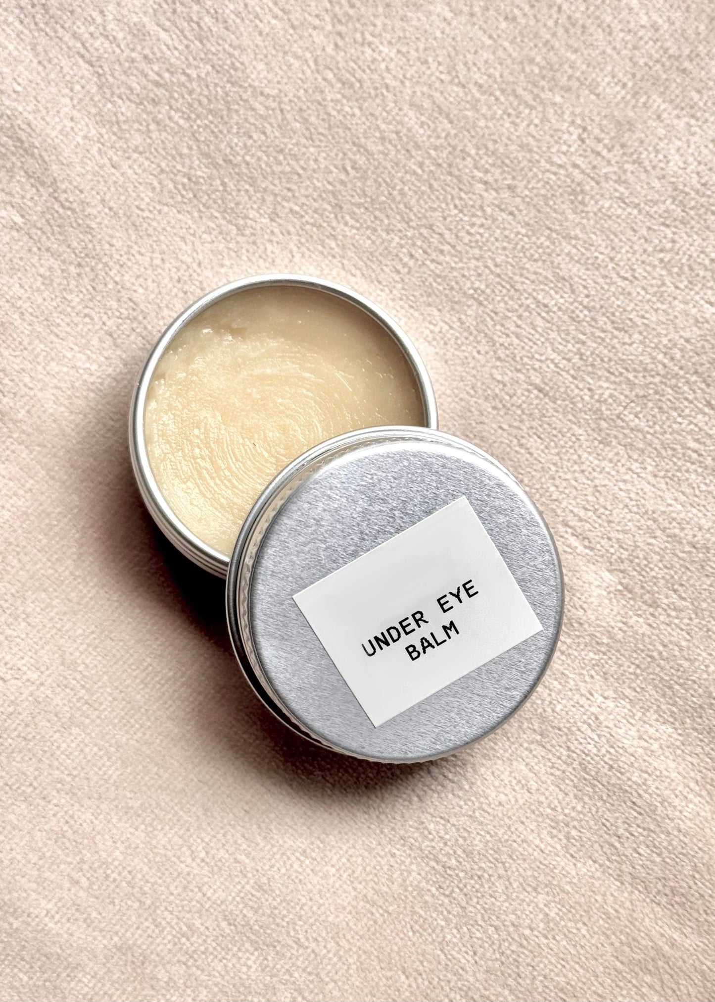 Open tin of under eye balm with a label on a beige background