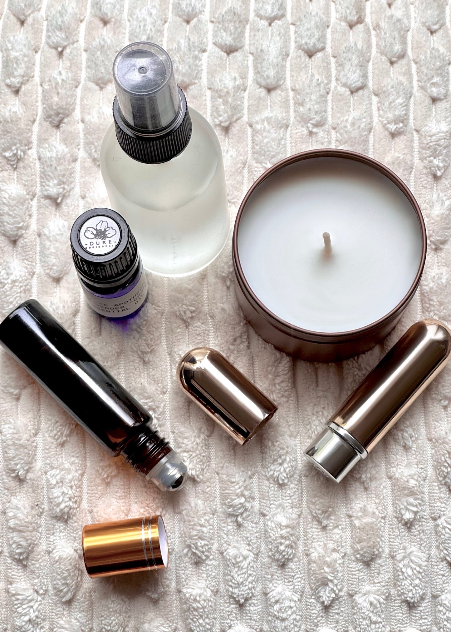 Collection of skincare and wellness products including a candle, bottles, and roller balls on a textured white surface.