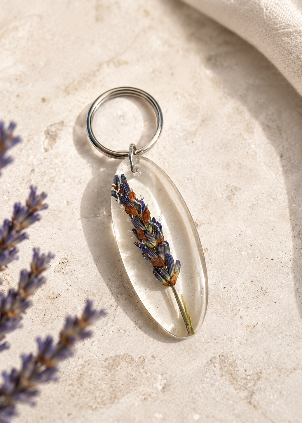 Keychain with a lavender flower inside a clear resin pendant on a light stone surface.