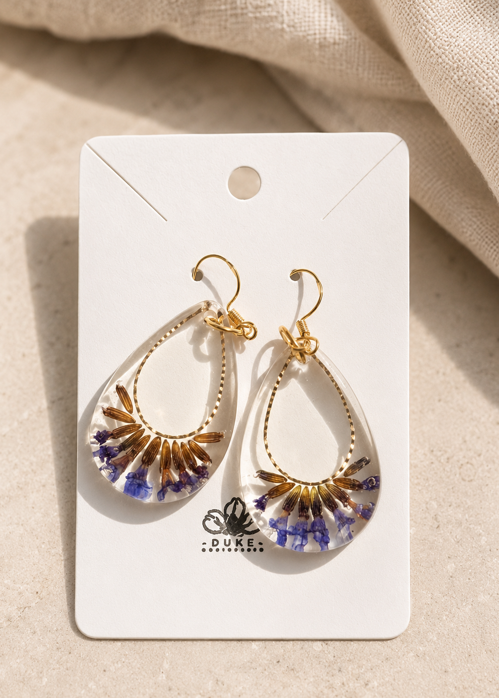 Pair of floral earrings on a Duke & Company branded card against a beige fabric background
