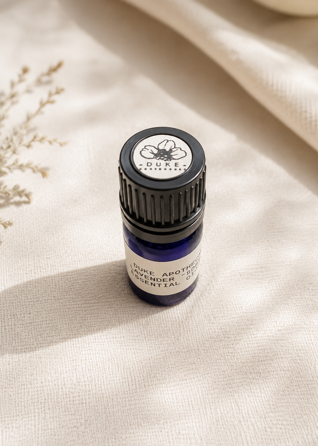 Essential oil bottle labeled 'Duke Apothecary' on a beige fabric background