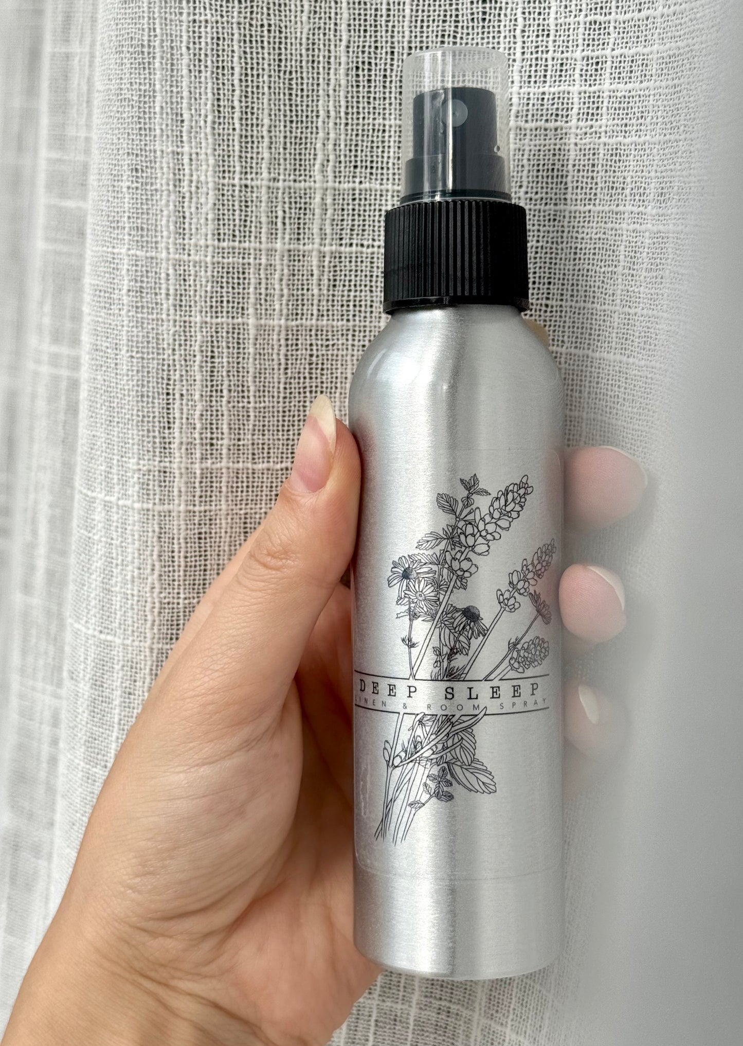 Hand holding a silver spray bottle with black cap against a textured gray background
