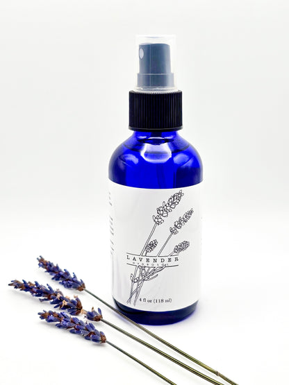 A blue spray bottle labeled 'Lavender' next to a sprig of lavender, indicating the product is a lavender hydrosol with a spray application.
