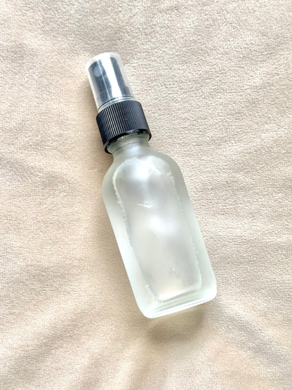 Clear glass spray bottle with black nozzle on a beige fabric background