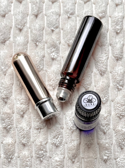 Two silver rollerball bottles and a small round bottle with a visible brand logo on a textured white surface.