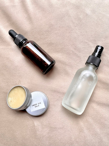Skincare products including a dropper bottle, spray bottle, and jar on a beige surface.